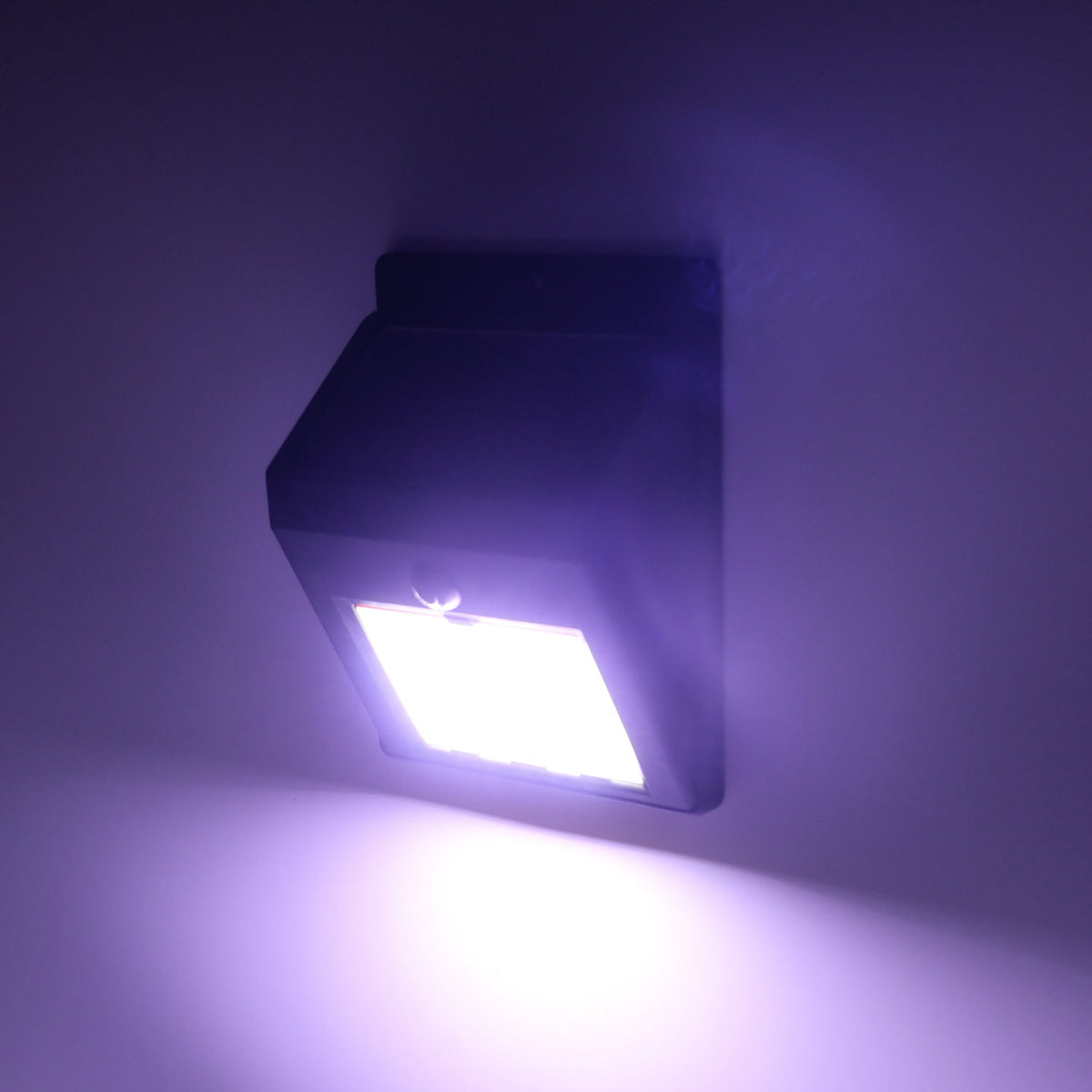 Black solar-powered wall light with 30 LEDs emitting a bright white light onto a purple-hued wall in the dark.