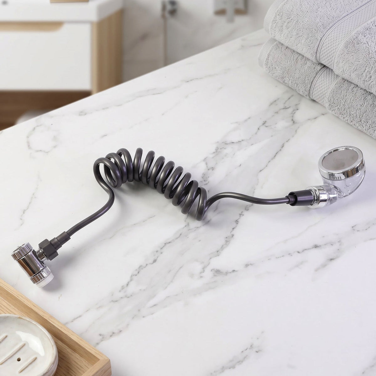 The coiled grey hose and shower spray head rest on a white marble countertop next to folded grey towels.