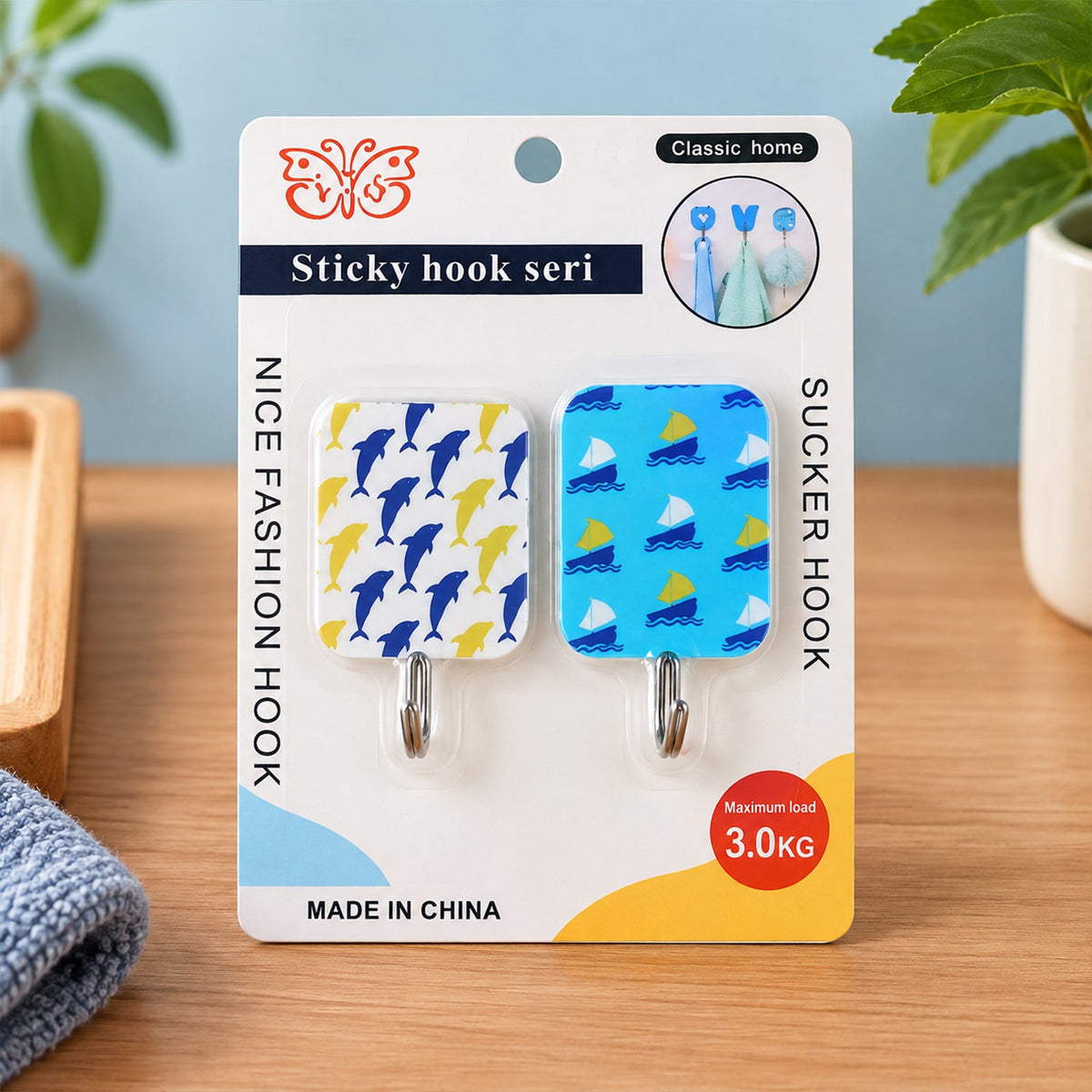 Two patterned adhesive hooks, one with blue dolphins and one with blue sailboats, displayed in packaging on a wooden surface.