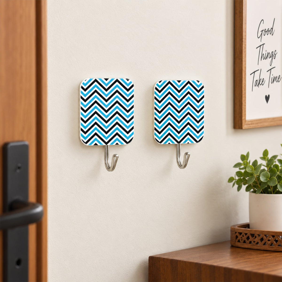 Two blue and black chevron-patterned adhesive hooks are mounted on a light wall next to a wooden door and a framed picture.