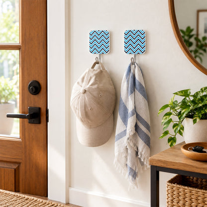 Two chevron-patterned adhesive hooks hold a beige baseball cap and a striped scarf near a wooden door and round mirror.
