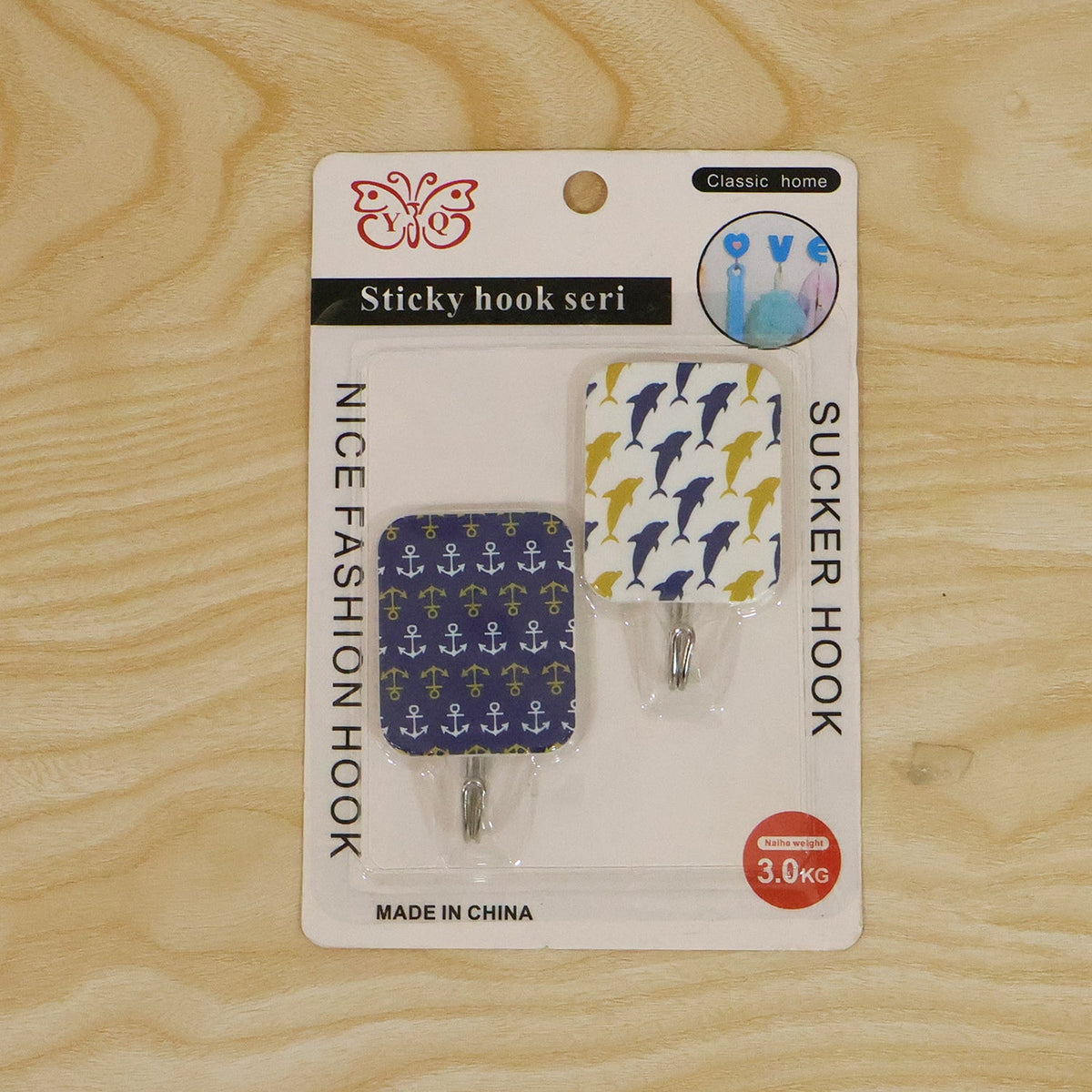 Two patterned adhesive hooks in their retail packaging, featuring blue dolphins and yellow anchors, on a wooden surface.