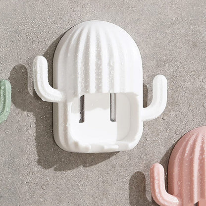 White cactus toothbrush holder covered in water droplets, mounted on a wet gray tiled wall next to a pink one.
