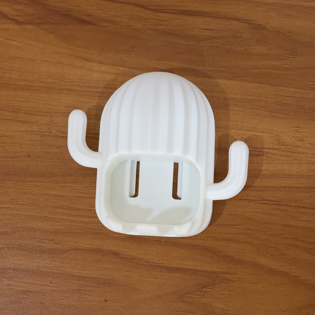 White cactus toothbrush holder with two slots, resting on a light brown wooden surface.