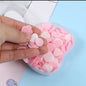 A hand holds several pink and white heart and circle-shaped paper soap pieces above an open apple-shaped container.