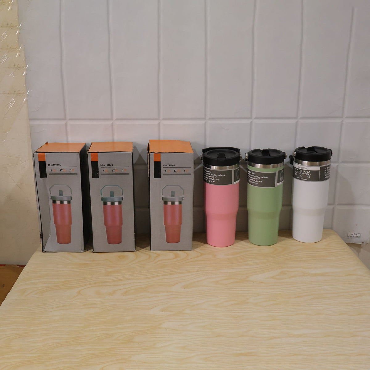 Three boxed pink tumblers and three unboxed tumblers in pink, green, and white sit on a wooden table.