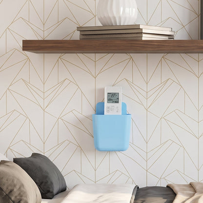 A light blue wall-mounted plastic storage pocket holds a white remote control against a geometric patterned wall above a bed.