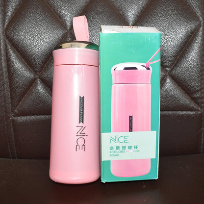 A pink vacuum flask with a silver lid and strap stands next to its retail box on a dark brown quilted surface.