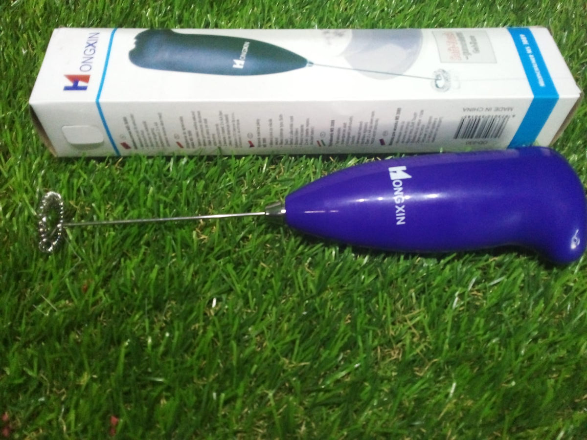 A purple frother and its white and blue packaging box are displayed on a vibrant green grass background.