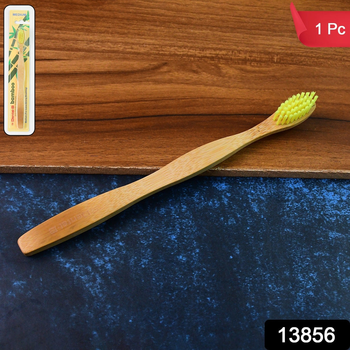 A single bamboo toothbrush with yellow bristles rests on a two-toned wooden surface.