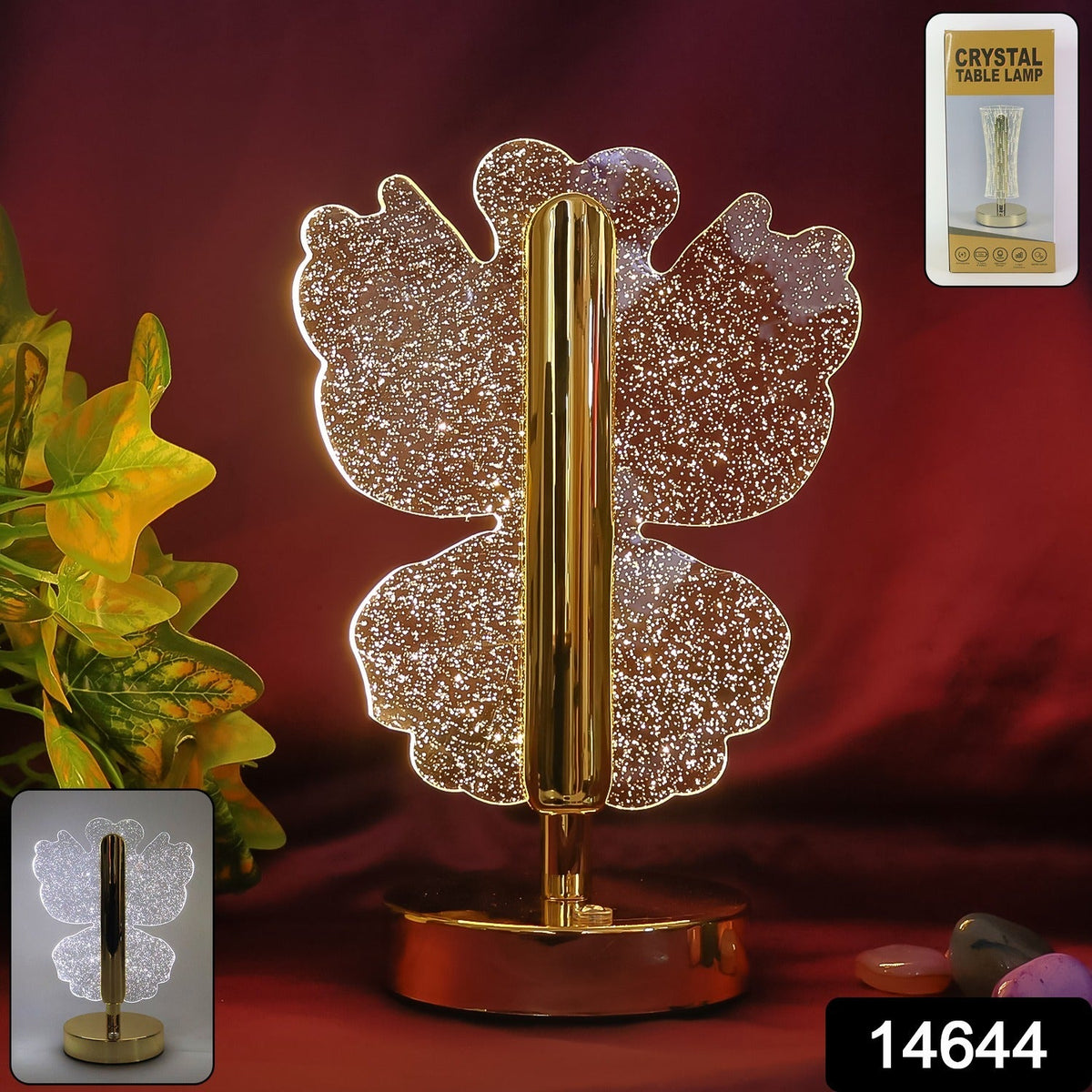 A glowing crystal butterfly lamp with a gold stem and base, against a dark red background with green foliage.