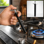 A hand holds a black and silver gas lighter, igniting a blue flame on a stainless steel stovetop burner.