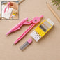 A pink compass, yellow eraser with brush, and lead refills on a wooden desk with a notebook and pencil.