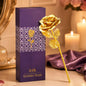 A gold-plated rose stands next to a purple gift box with a patterned design and gold text.