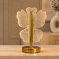 A glowing crystal butterfly-shaped table lamp with a gold base and stem, on a light-colored surface.