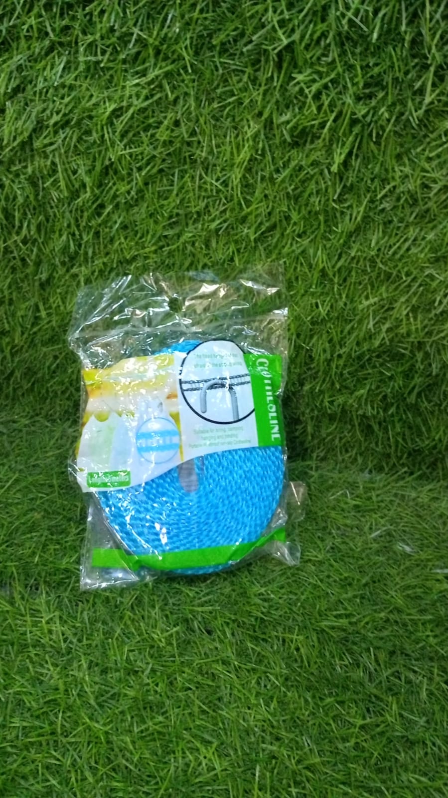 A packaged blue clothesline with product information is lying on a vibrant green artificial grass surface.