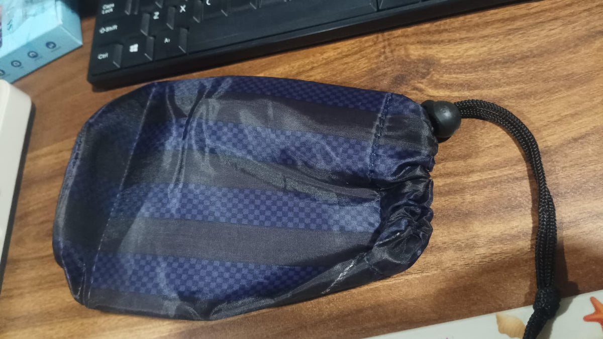 A navy blue drawstring pouch with vertical stripes lies flat on a wooden desk next to a black keyboard.