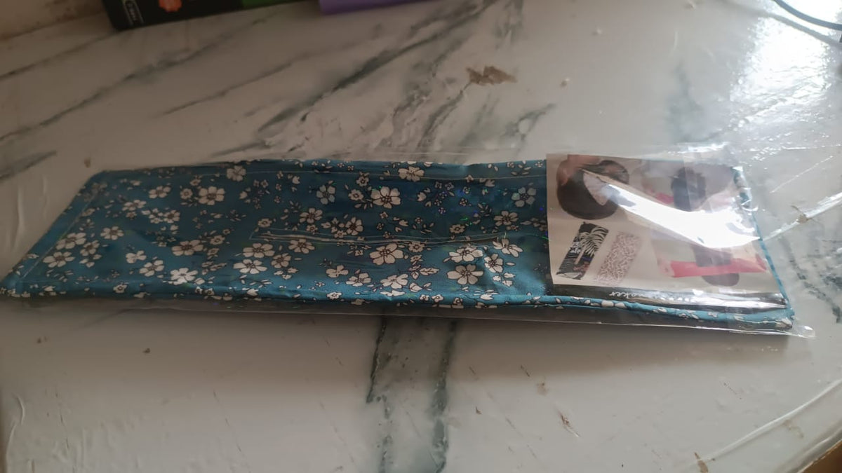A blue floral hair bun maker in clear plastic packaging on a patterned table.