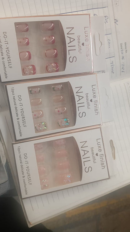 Three boxes of Luxe Finish Beautiful Nails, each containing 12 nude press-on nails with different designs, on a desk.