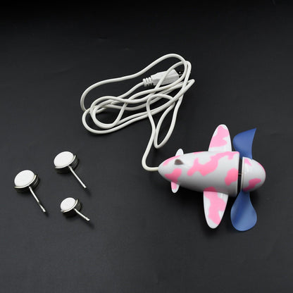 A pink and white airplane USB fan with blue propellers and three small white and silver wheels on a dark surface.
