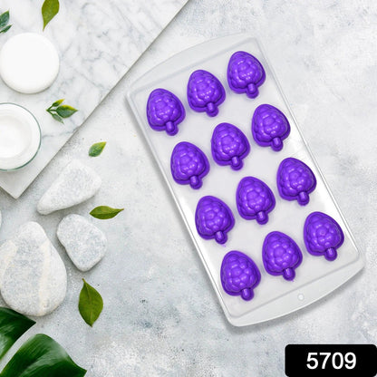 Purple silicone fruit-shaped ice cube tray on a white marble surface with white stones and green leaves.