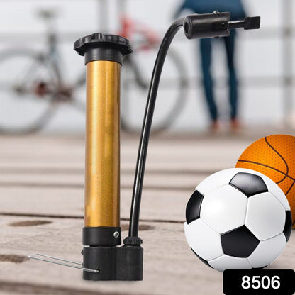 A gold and black hand pump stands next to a soccer ball and a basketball, with a bicycle in the background