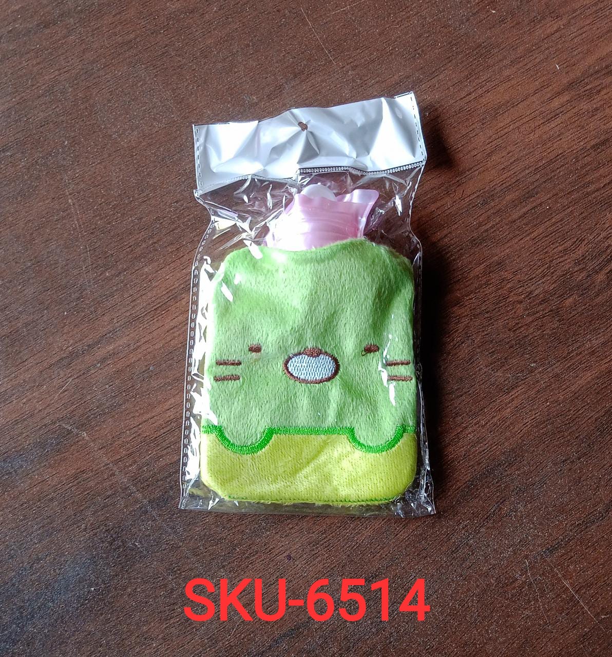 A green and yellow kitty hot water bag with a pink top is sealed in clear plastic packaging.