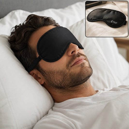 A man with a beard sleeps peacefully on a white pillow, wearing a black sleeping eye mask with an adjustable strap.