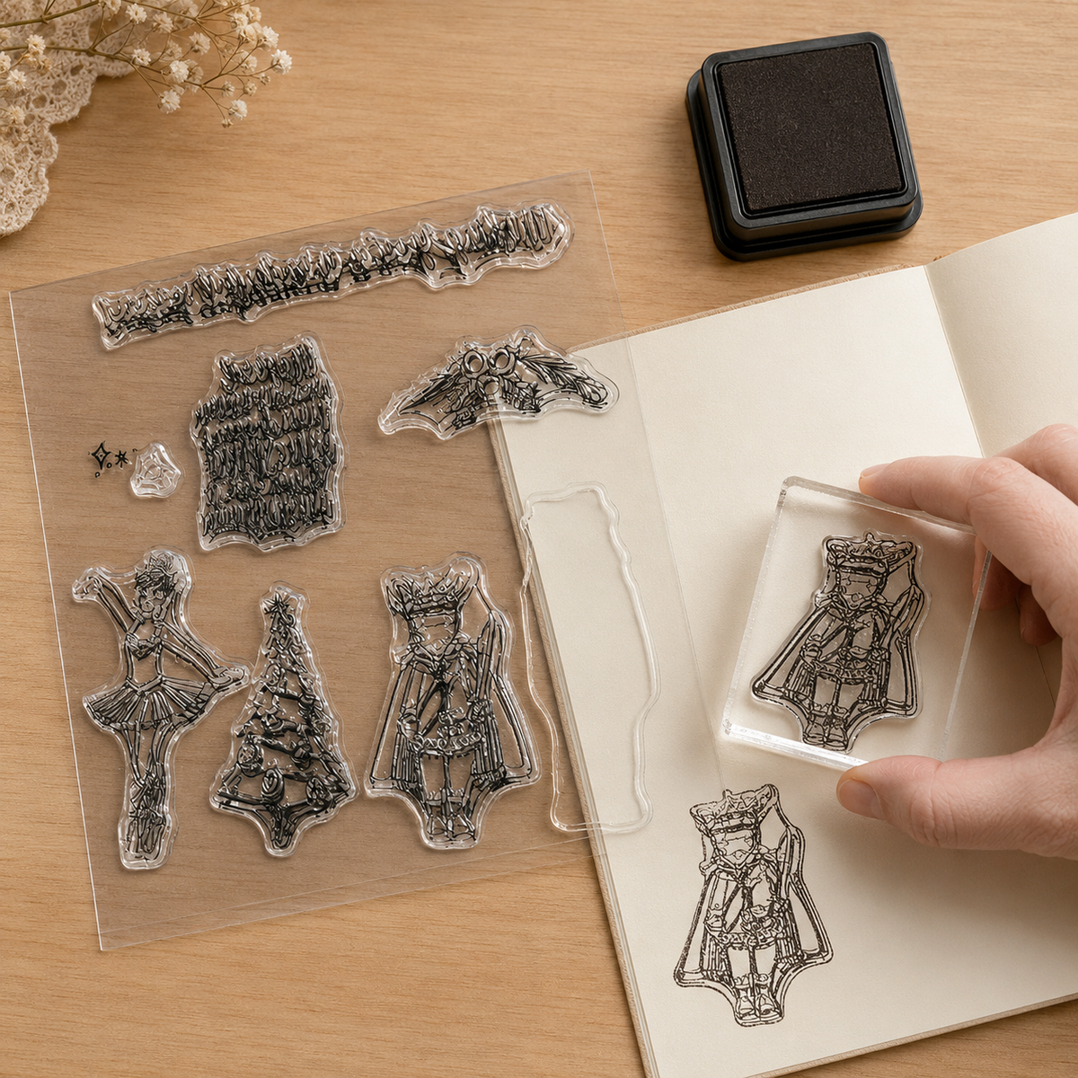 A hand holds a clear stamp of a crown over a notebook, next to a sheet of various clear stamps and an ink pad.