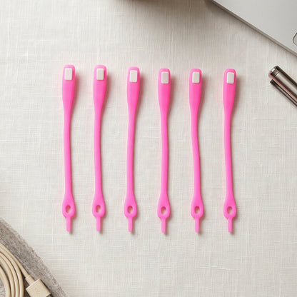 Six bright pink silicone no-tie shoelaces with white clasps, neatly arranged on a white textured surface next to a laptop.