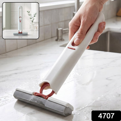 A hand holding a white and red mini mop with a grey sponge head, cleaning a wet white countertop. – view 2