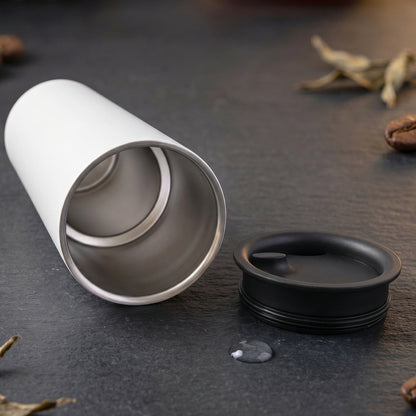 An open white thermal tumbler with a stainless steel interior and its black lid resting on a dark surface.