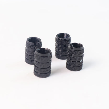 Four black, textured, cylindrical valve caps standing upright on a white background.