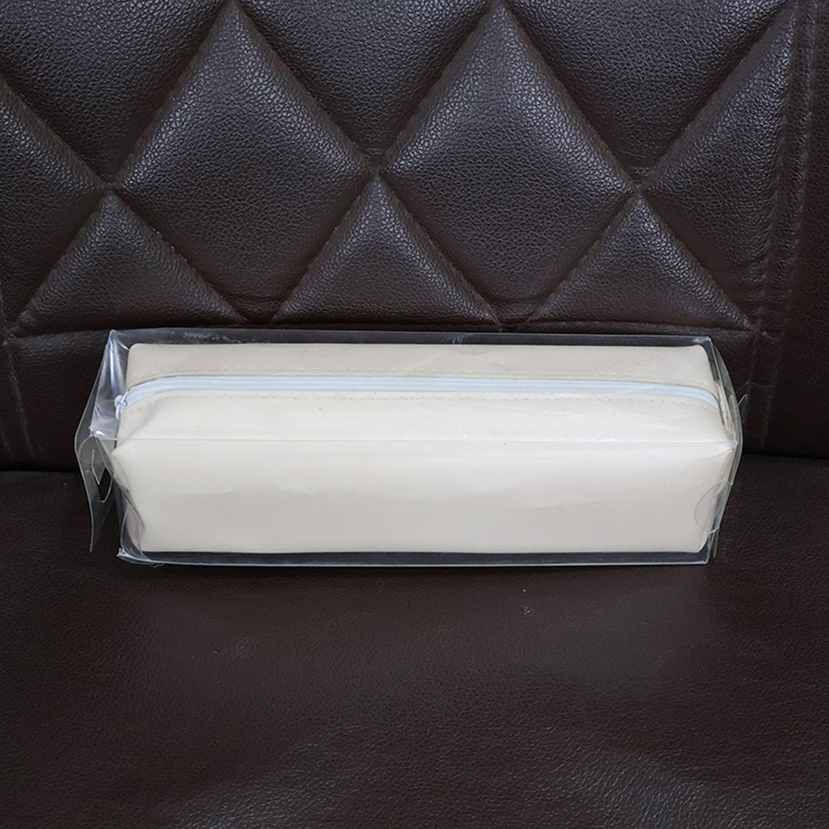 Beige pencil case in clear plastic packaging, resting on a brown quilted leather surface.